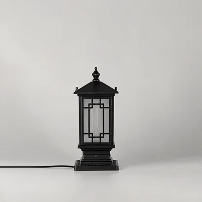 A black outdoor lantern-style table lamp with a square base and geometric glass panels, shown on a light gray studio background with its power cord extending to the left.