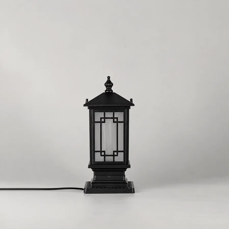 A black outdoor lantern-style table lamp with a square base and geometric glass panels, shown on a light gray studio background with its power cord extending to the left.
