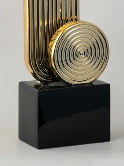 Detailed closeup of gold metal abstract sculpture with circular pattern on black base for modern interiors.