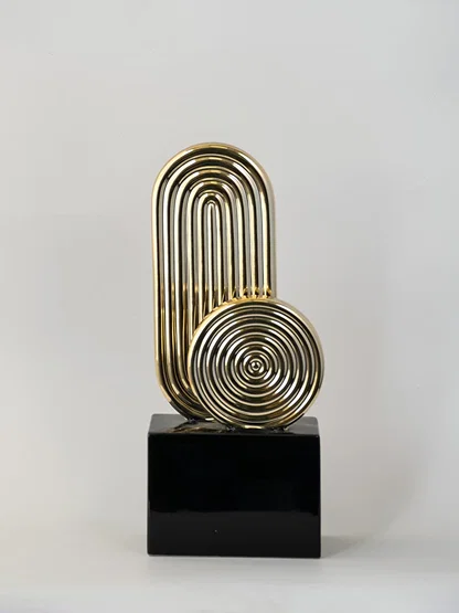 Gold metal decorative sculpture on black base for table placement with modern design on white background.